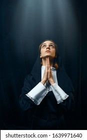 Nun in a cassock prays on light over her head