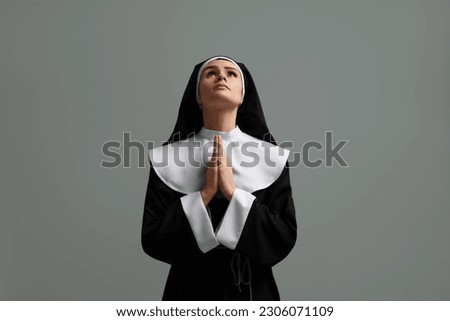 Nun with clasped hands praying to God on grey background
