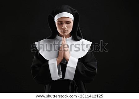 Nun with clasped hands praying to God on black background