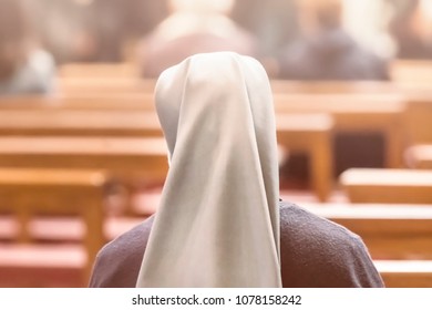 A nun is sitting on a bench during a church service, the view from the back