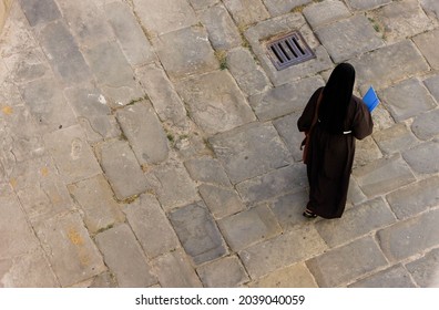 Nun walking along the street of a medieval city, top view 