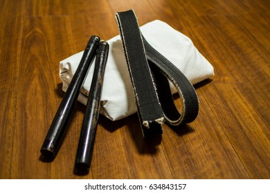 Nunchaku (traditional Okinawa Kenpo Karate's Weapon), Black Belt (Karate, Judo, Kenpo, Jiu-Jitsu, Budo, Martial Arts, Taekwondo) And Gi (Japanese Martial Arts Uniform) On The Wood Floor