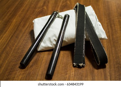 Nunchaku (traditional Okinawa Kenpo Karate's Weapon), Black Belt (Karate, Judo, Kenpo, Jiu-Jitsu, Budo, Martial Arts, Taekwondo) And Gi (Japanese Martial Arts Uniform) On The Wood Floor