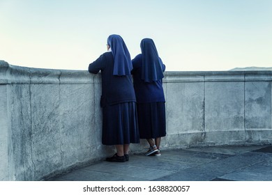 Nuns in black dresses look at the sea from the balcony of Notre Dame in Marseille. Back view.
