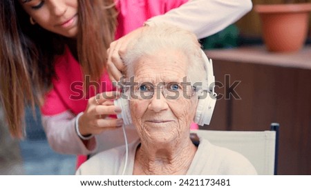 Nurse adjusting headphones to a senior woman in a geriatric