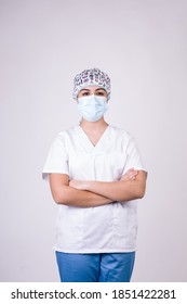 Nurse With Arms Crossed On White Background. She Is Wearing A Mask And A Hat To Protect Herself From The Coronavirus.