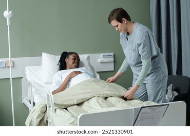 Nurse assisting Black pregnant woman in hospital bed, ensuring her comfort in medical setting with green walls and medical equipment, filled with compassion and dedication - Powered by Shutterstock