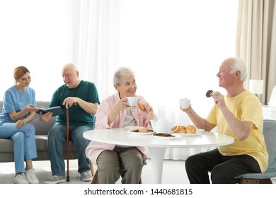 Nurse assisting elderly man while senior couple having breakfast at retirement home