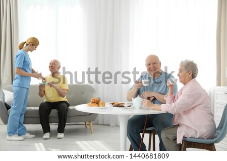 Nurse assisting elderly man while senior couple having breakfast at retirement home