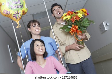 Nurse Assisting Female Patient On Wheelchair While Leaving Hospital With Man