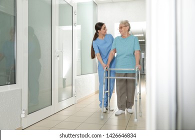 Nurse Assisting Senior Patient With Walker In Hospital Hallway