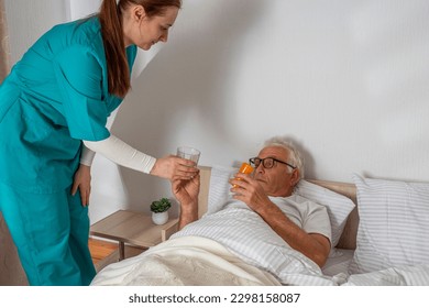 Nurse brought pills to elderly man at his home. Solicitous professional medical female staff caring in a geriatric institution with a senior patient. Lifestyle nursing service.