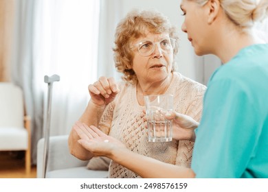 Nurse caring for a senior woman at home, giving medication with water. Showcasing trust and professionalism in healthcare - Powered by Shutterstock