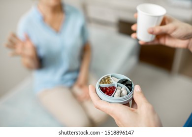 Nurse Carrying Water And Pill Box With Medicine For A Senior Woman, Taking Care Of An Elder Patient Indoors, Close-up View