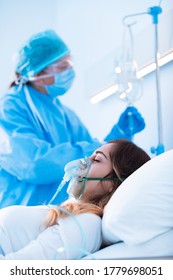 Nurse Checking A Intravenus Drip On An Ill Patient Wearing A Positive Pressure Oxygen Mask In Hospital During The Covid-19 Pandemic In A Close Up Profile View Of The Woman