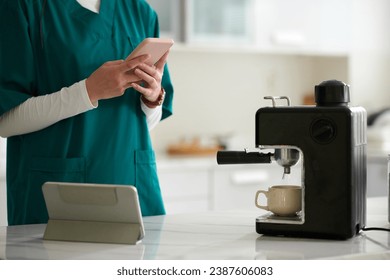 Nurse checking notifications on social media when making morning coffee - Powered by Shutterstock