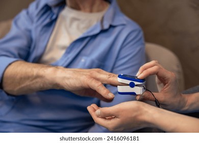 Nurse checking pulse or level of oxygen using oximeter of unrecognizable senior man.