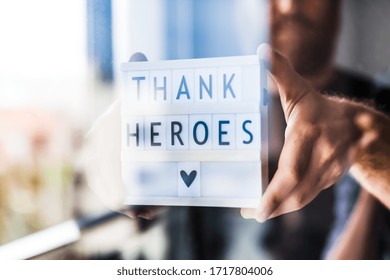 Nurse day concept. Man hands holding lightbox with Thank heroes text thanking doctors, nurses and medical staff working in hospitals during coronavirus COVID-19 pandemics. View through window glass