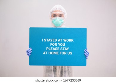 Nurse With Disposable Coverall And Mask Wearing Safety Glasses Holding A Sign Stay At Home. Pandemic 2019 Coronavirus 2019-nCoV.