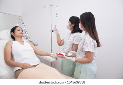 Nurse Or Doctor Preparing And Adjusting Infusion Or Chemotherapy Drip For Asian Woman Patient In Hospital Or Beauty Salon. Healthcare And Medicine Concept