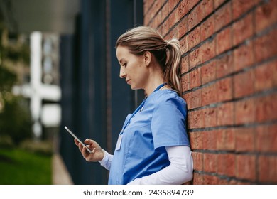 Nurse, doctor in uniform taking break, standing in front hospital building, scrolling on smartphone. Work-life balance of healthcare worker. - Powered by Shutterstock