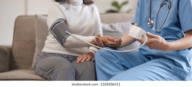 nurse doctor using digital tonometer check blood pressure for old asia female at home in elderly care cardiovascular medical visit, cholesterol problem. Home health care and nursing home concept