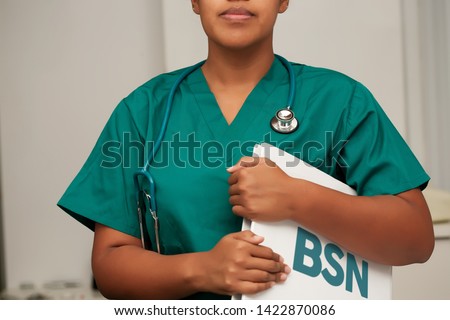 A nurse enrolled in a Bachelor of Science in Nursing degree program, holding a binder in her arms and wearing a stethoscope.