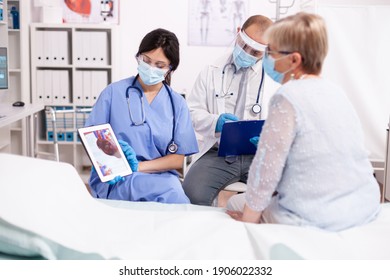 Nurse explaining heart diagnosis in cardiology to senior woman on tablet pc in time of covid pandemic. Medical assistant having a conversation with elder patient during coronavirus outbreak.