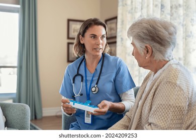 Nurse Explaining Medicine Dosage To Old Patient In Care Facility Centre While Holding Weekly Medicine Dispenser. Caregiver Holding Pill Organizer Box Giving Medicine Tablet To Elderly Woman.