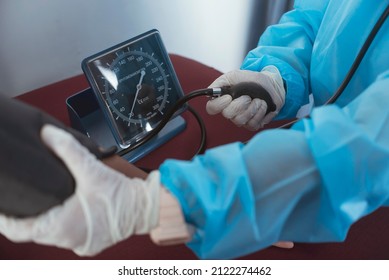 A Nurse In Full PPE Gear Inflating A Cuff To Check The Blood Pressure. Using A Sphygmomanometer. At The ER Or Emergency Room Of A Hospital.