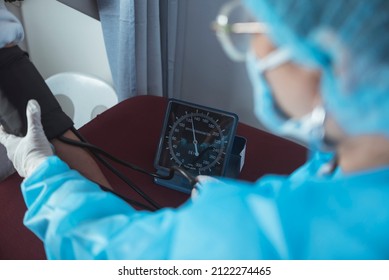 A Nurse In Full PPE Gear Inflating A Cuff To Check The Blood Pressure. Using A Sphygmomanometer. At The ER Or Emergency Room Of A Hospital.