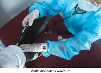 A Nurse In Full PPE Gear Straps On A Inflatable Cuff On A Patient At An ER. Checking Blood Pressure With A Sphygmomanometer