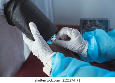 A Nurse In Full PPE Gear Taking Blood Pressure At The Brachial Artery. Inserting A Stethoscope Inside The Inflatable Cuff. At The ER Or Emergency Room Of A Hospital.