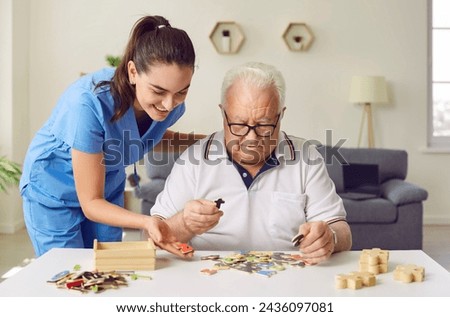 Nurse in geriatric clinic or retirement home helping patient with alphabet puzzle. Senior man sitting at desk and playing games with letters. Old age, dementia, Alzheimer's disease, therapy concept