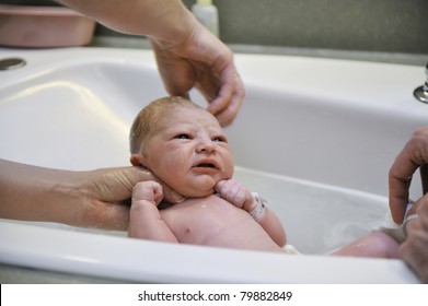 A Nurse Gives A Newborn Baby His First Bath With Dad Helping.