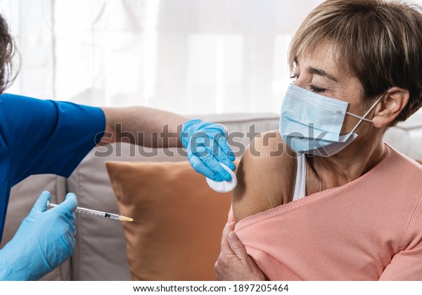 Nurse giving coronavirus vaccine to senior woman\
inside home during lockdown isolation - Covid-19 injection to\
patient concept - Focus on\
hand