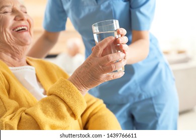 Nurse giving glass of water to senior woman indoors, closeup. Assisting elderly people - Powered by Shutterstock