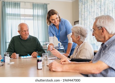 Nurse Giving Medicine To Group Of Seniors At Retirement Community. Happy Smiling Nurse Gives Medicines To Elderly Patients At Nursing Home. Happy Senior Woman Taking Her Dose Of Medicines.