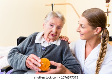 Nurse Giving Physical Therapy With Massage Ball To Senior Woman In Wheelchair