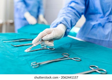 Nurse hand taking surgical instrument for group of surgeons at background operating patient in surgical theatre. Steel medical instruments ready to be used. Surgery and emergency concept