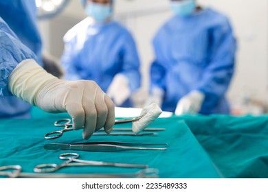 Nurse hand taking surgical instrument for group of surgeons at background operating patient in surgical theatre. Steel medical instruments ready to be used. Surgery and emergency concept - Powered by Shutterstock