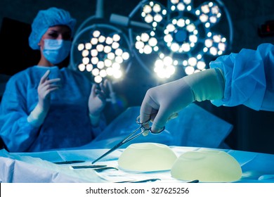 Nurse hand taking surgical instrument for group of surgeons at background operating patient .  breast augmentation.