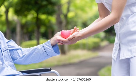 Nurse Handing Over Hearts Icon To Old Patient In Wheelchair At Park