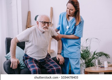 Nurse Helping Old Man To Stand Up From Chair