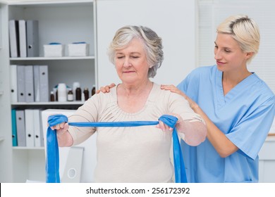 Nurse helping senior patient in exercising with resistance band in clinic
