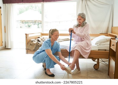 Nurse helping senior woman get up and putting on slippers in nursing home - Powered by Shutterstock