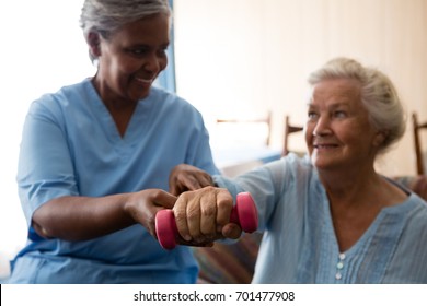 Nurse Helping Senior Woman In Lifting Dumbell At Retirement Home