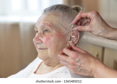 a nurse helps a 90 year old grandmother insert a hearing aid into her ear - Powered by Shutterstock