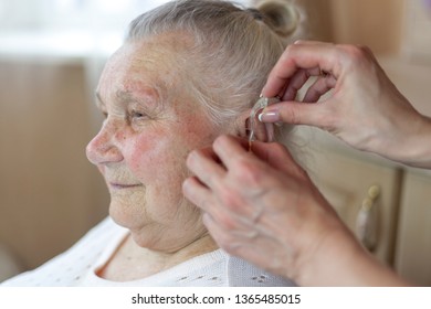 a nurse helps a 90 year old grandmother insert a hearing aid into her ear - Powered by Shutterstock