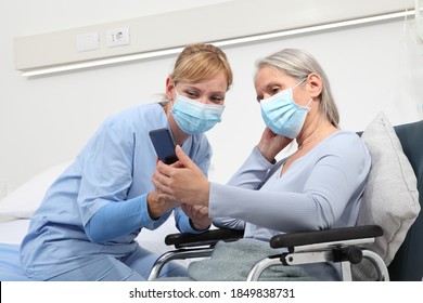 nurse helps with cell phone to contact the elderly lady's family in the wheelchair, wearing surgical protective medical masks in hospital room, concept of isolation from corona virus covid 19